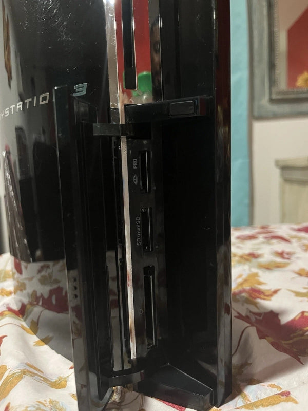 Black gaming console on a bed with a colorful blanket